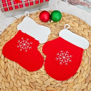 May include: Two red and white crocheted Christmas stocking ornaments with white snowflake embroidery. The ornaments are on a woven wicker placemat.