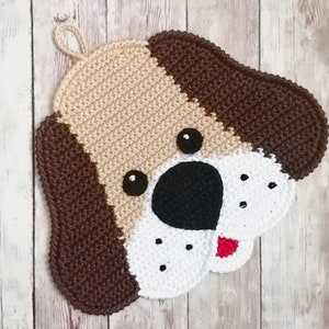 May include: A crocheted dog-shaped pot holder with brown, beige, white, and red yarn. The pot holder has a loop for hanging.