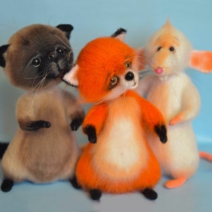 May include: Three handmade felted animal toys: a brown and white cat, an orange and white fox, and a white mouse with pink ears. The toys are standing on a light blue background.