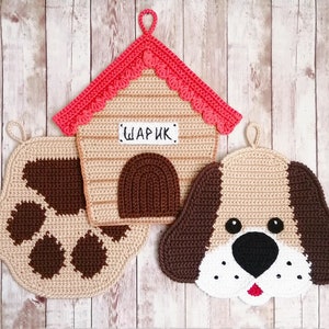 Puede incluir: Tres posavasos de ganchillo en forma de caseta de perro, una huella de pata y una cara de perro. La caseta de perro es beige con un techo rojo y la palabra "шарик" escrita en la parte delantera. La huella de pata es beige con una huella de pata marrón en el centro. La cara del perro es beige con orejas marrones y una nariz negra.