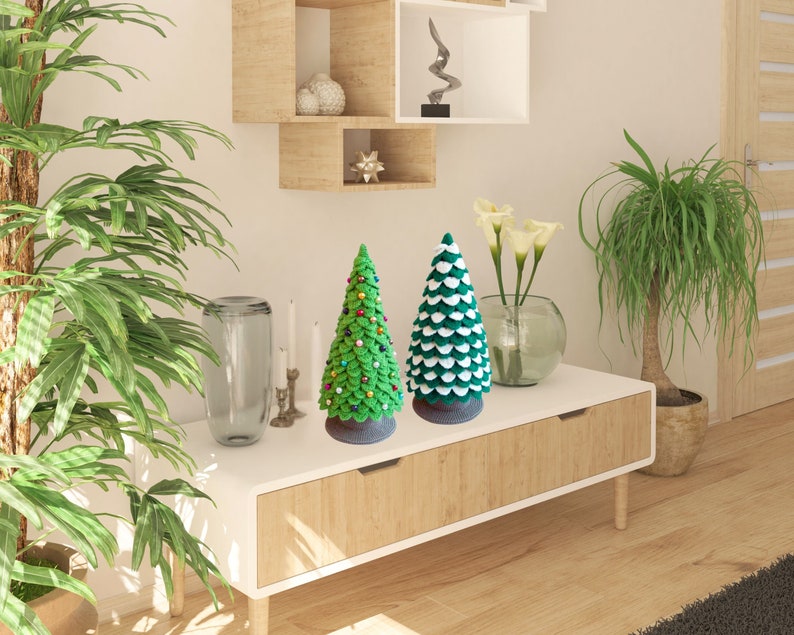 May include: Two green and white felt Christmas trees on a wooden shelf with a white top. The tree on the left has red and gold ornaments. The tree on the right has white accents.