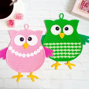 Könnte beinhalten: Zwei gehäkelte Eulen-Topflappen, einer rosa und einer grün. Beide Eulen haben große weiße Augen und einen gelben Schnabel.