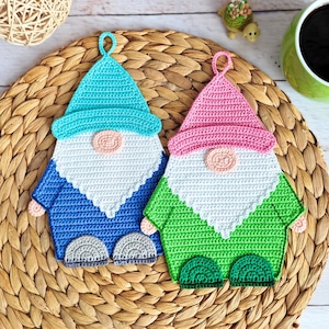 May include: Two handmade crochet gnome pot holders. One gnome is blue and white with a turquoise hat, the other is green and white with a pink hat. Both have a light pink nose and gray feet. They are on a woven placemat.