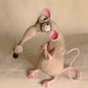 Pode incluir: Um brinquedo de rato cinza de croch&ecirc; com orelhas cor-de-rosa e olhos saltados grandes. O rato tem uma cauda longa e encaracolada.