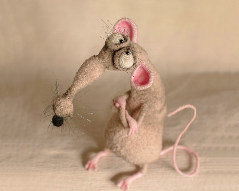 Pode incluir: Um brinquedo de rato cinza de croch&ecirc; com orelhas cor-de-rosa e olhos saltados grandes. O rato tem uma cauda longa e encaracolada.