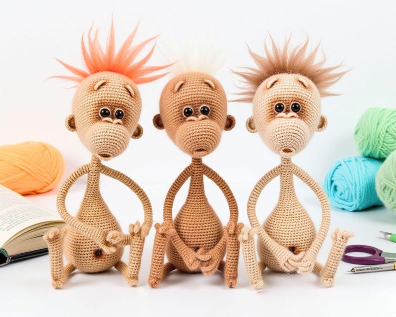 May include: Three crocheted monkey toys with different colored hair. The monkey on the left has orange hair, the middle monkey has white hair, and the monkey on the right has brown hair. All three monkeys are sitting on a white surface.