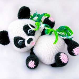 Może przedstawiać: Pluszowa zabawka panda wykonana na szydełku z czarno-białym futerkiem, zielonymi liśćmi i różowymi akcentami. Panda leży na boku z głową odwróconą.