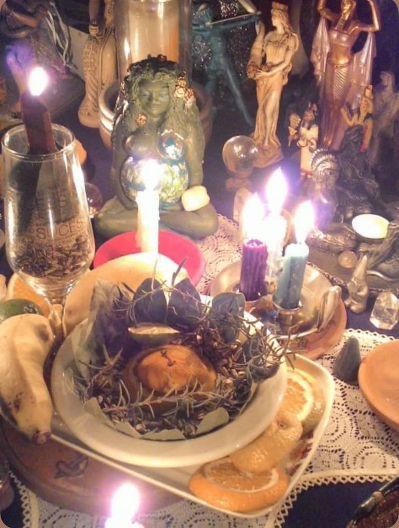 Puede incluir: Un cuenco de cer&aacute;mica blanca con hierbas secas y una fruta redonda, colocado sobre un plato blanco con rodajas de c&iacute;tricos. La escena incluye una figura de diosa verde, un vaso con una vela encendida y varias otras velas encendidas.