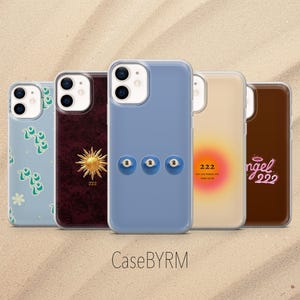 以下が含まれることがあります： 一列に並んだ5つのスマートフォンケース。1つ目は緑の花柄のライトブルー。2つ目は金色の太陽と数字の222が描かれたダークレッド。3つ目は2と書かれた3つのビリヤードボールが描かれたブルー。4つ目はピンクとオレンジのグラデーションに222とテキスト。5つ目はangel 222のテキストがあるブラウン。下にCaseBYRMのテキスト。