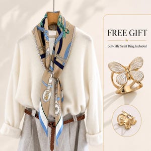 May include: A beige scarf with blue and navy ribbon patterns, worn with a gold-toned butterfly scarf ring. The text FREE GIFT and Butterfly Scarf Ring Included appear next to the accessory, which features white enamel wings and a gold metal band.