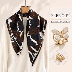May include: A square scarf featuring a brown and black animal print pattern with white accents, draped over a white shirt. The set includes a gold-toned butterfly scarf ring with white enamel wings, as shown in the text labelled FREE GIFT.