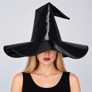 May include: A black witch hat with a glossy, patent-like finish. The hat features a tall, pointed crown that bends slightly at the top and a wide, circular brim with stitched edges. The material has a reflective surface that catches light.