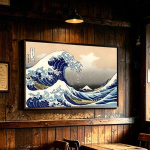 Peut inclure: Une impression encadrée de La Grande Vague de Kanagawa représentant une grande vague bleue stylisée avec des crêtes d'écume blanche, plusieurs bateaux et un sommet de montagne lointain sur un fond beige, fixée sur un mur en bois sombre.