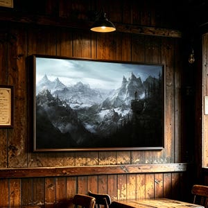 May include: A rectangular framed wall art print featuring a dark, atmospheric landscape of snow-capped mountains, jagged cliffs, and a lone figure standing on a rocky precipice, all set against a cloudy, overcast sky with deep shadows and mist.