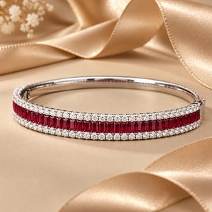 Puede incluir: Una pulsera rígida articulada de metal plateado pulido, con una fila central de rubíes de color rojo intenso en talla rectangular, flanqueada por dos filas paralelas de pequeñas piedras blancas redondas y transparentes.