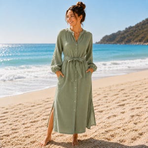 Op de afbeelding: Een saliegroene maxi-jurk met lange mouwen, een knoopsluiting aan de voorzijde, een kraag en een bijpassende strikceintuur in de taille. De jurk heeft lange mouwen met manchetten, steekzakken aan de zijkanten en hoge zijsplitten in de zoom.