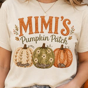 May include: A cream-colored t-shirt featuring the text "MIMI'S Pumpkin Patch" in orange and green. Below the text are three illustrated pumpkins in cream, green, and orange, each labeled with the names "Sawyer," "Oaklynn," and "Ella."