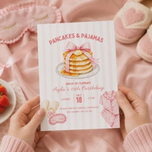 Puede incluir: Una tarjeta de invitación de cumpleaños rectangular con un fondo de rayas rosa claro y blanco. El texto dice PANCAKES & PAJAMAS, JOIN US TO CELEBRATE Ayla's 12th Birthday, SATURDAY JULY 18, 2-5 PM, 245 BRICKSTONE LANE, TOWN MESA, ARIZONA 85201, RSVP TO MOMMY AT 607-556-1042. Incluye ilustraciones de una pila de tortitas con un lazo rosa, zapatillas, un antifaz para dormir y un pijama.