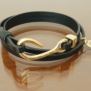 May include: A black leather wrap bracelet with a gold hook clasp and a small gold charm with the text "Lilly's Allure".