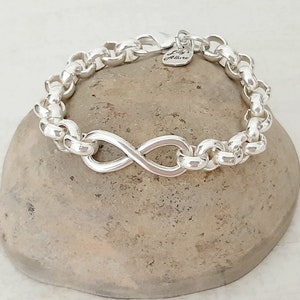 May include: Silver infinity bracelet with a chain link design. The bracelet has a small heart-shaped tag with the text "Lily's Allure" on it.