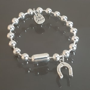 May include: A silver bracelet with a horseshoe charm and a silver tag that reads "Lilly's Allure".