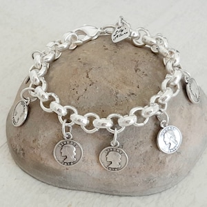 May include: Silver charm bracelet with a chain link design and multiple silver coin charms. The coin charms feature a profile of a woman's face and the text "LIBERTY 1916".