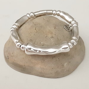 May include: Silver bracelet with a large, textured, curved bar and smaller beads. The bracelet has a magnetic clasp.