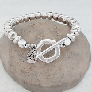 May include: Silver beaded bracelet with a toggle clasp and a small heart charm that says "Lilly's Allure".