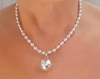 May include: A silver necklace with a large, round pendant. The necklace is made of small, round beads.