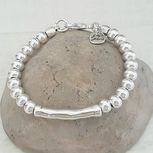 May include: Silver beaded bracelet with a silver bar charm and a small heart-shaped charm that says "Lilly Allure".