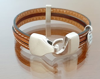 May include: A brown leather bracelet with two brown leather straps and a silver clasp. The bracelet has a small silver charm with the text "Lily & Milo" on it.