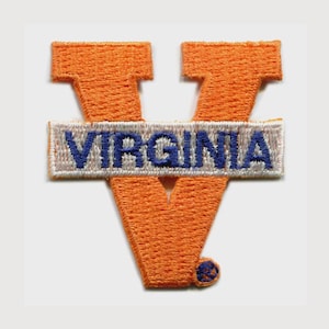 May include: An embroidered patch featuring a large orange letter V with a horizontal white rectangular bar across the center. The word VIRGINIA is stitched in blue capital letters on the white bar, and a small blue circular accent is at the base.