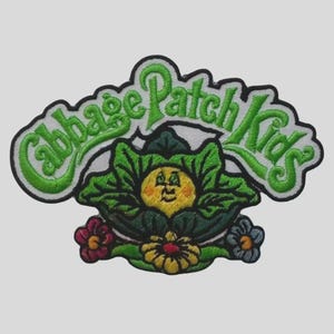 May include: Embroidered patch with the text "Cabbage Patch Kids" in green, depicting a smiling face surrounded by green leaves and flowers. The patch has a black border.