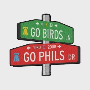 May include: Embroidered signpost patch with green and red street signs. The green sign reads "GO BIRDS LN" with a bell graphic and "41 E 33" arrows. The red sign says "GO PHILS DR" with a bell graphic and "1980 E 2008" arrows.