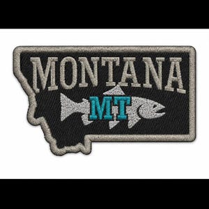 Puede incluir: Un parche bordado negro con la forma del estado de Montana y un borde gris claro. El parche presenta el texto blanco MONTANA sobre una silueta de pez blanca que contiene las letras azul brillante MT en el centro del cuerpo del pez.