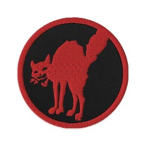Puede incluir: Parche bordado con una silueta de gato rojo sobre un fondo circular negro. El gato está arqueado con la cola levantada, y el parche tiene un borde rojo. El diseño es una representación estilizada de un gato.