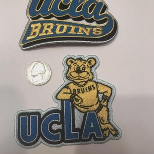 May include: Two embroidered patches featuring the UCLA Bruins logo and mascot. The top patch displays "UCLA BRUINS" in blue and gold lettering. The bottom patch shows the UCLA bear mascot and the word "UCLA" in blue.