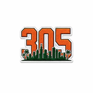 Op de afbeelding: Een geborduurde patch met de oranje cijfers 305 met een witte rand. Onder de cijfers staat een donkergroen silhouet van een stadsskyline en palmbomen. Het ontwerp is geplaatst tegen een witte achtergrond met een gestikte rand.