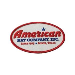 May include: Oval patch with a white background and a red border. The patch features the text "American" in red, "HAT COMPANY, INC." in blue, and "SINCE 1915 BOWIE, TEXAS" in blue. A blue star is above the text.