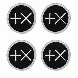 May include: Four circular patches with a black background and a white plus sign crossed with an X. Each patch has a white border.