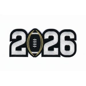 Könnte beinhalten: Gestickter Aufnäher mit der Jahreszahl "2026" und einem Football in der Mitte. Die Zahlen sind weiß mit schwarzem Rand, und der Football ist gold und weiß. Der Aufnäher ist für Sport- oder Schulkleidung gedacht.