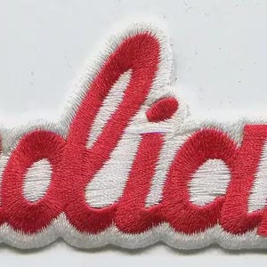 May include: Embroidered patch in the shape of the word "Indiana" in red script lettering with a white border. The patch has a textured appearance, with the red thread stitched onto a white fabric base.