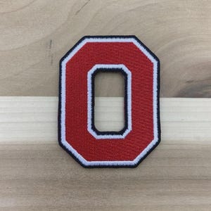 May include: Embroidered red letter "O" patch with a white border and black outline. The patch is in a bold, block letter style, perfect for adding to apparel or accessories. The patch is approximately 3 inches tall.