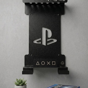 May include: A black metal wall-mounted storage rack for a PS4 console. The rack features a cutout PlayStation logo, the text PS4 at the top, and the controller symbols triangle, circle, cross, and square at the bottom, along with a small recycling icon.