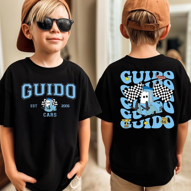 May include: A black t-shirt featuring a light blue graphic of the character Guido from Cars. The front displays the text GUIDO, EST 2006, and the character. The back features a large repeating GUIDO text pattern, the character, and checkered flags.