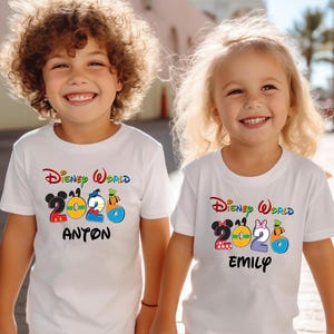 May include: Two children wearing white t-shirts with a colorful "Disney World 2026" design. One shirt has "Anton" printed below the design, the other has "Emily". The shirts feature Mickey and Minnie Mouse, and other Disney characters.