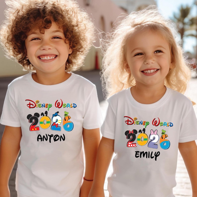 May include: Two children wearing white t-shirts with a colorful "Disney World 2026" design. One shirt has "Anton" printed below the design, the other has "Emily". The shirts feature Mickey and Minnie Mouse, and other Disney characters.