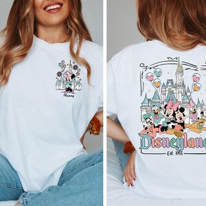 May include: A white t-shirt featuring a small graphic on the front left chest of Minnie Mouse in front of a castle with the text Mommy. The back displays a large graphic of Mickey, Minnie, Donald, Daisy, Goofy, and Pluto at a castle with Disneyland Est. 1955.
