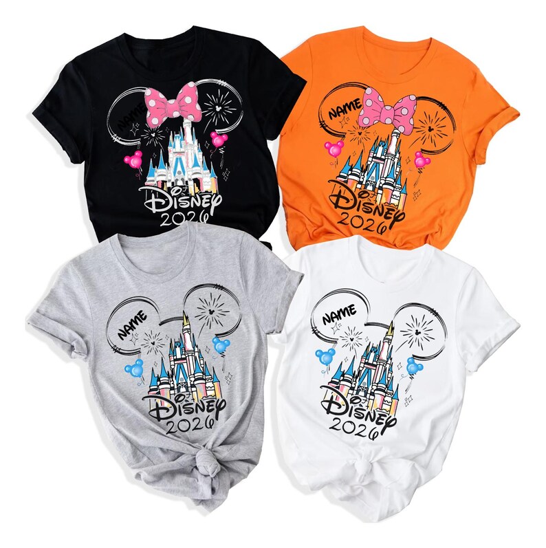 May include: Four short-sleeved t-shirts in black, orange, gray, and white. Each features a graphic of a castle, fireworks, and Mickey Mouse ears with a pink or blue bow. The text reads "NAME" and "Disney 2026" in a stylized black script font.