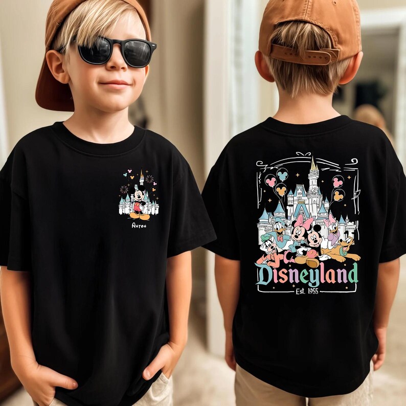 May include: A black t-shirt featuring a small graphic of Mickey Mouse and a castle on the front chest with the name Aaron, and a large graphic on the back showing Mickey, Minnie, Donald, Daisy, Goofy, and Pluto in front of a castle with Disneyland Est. 1955 text.